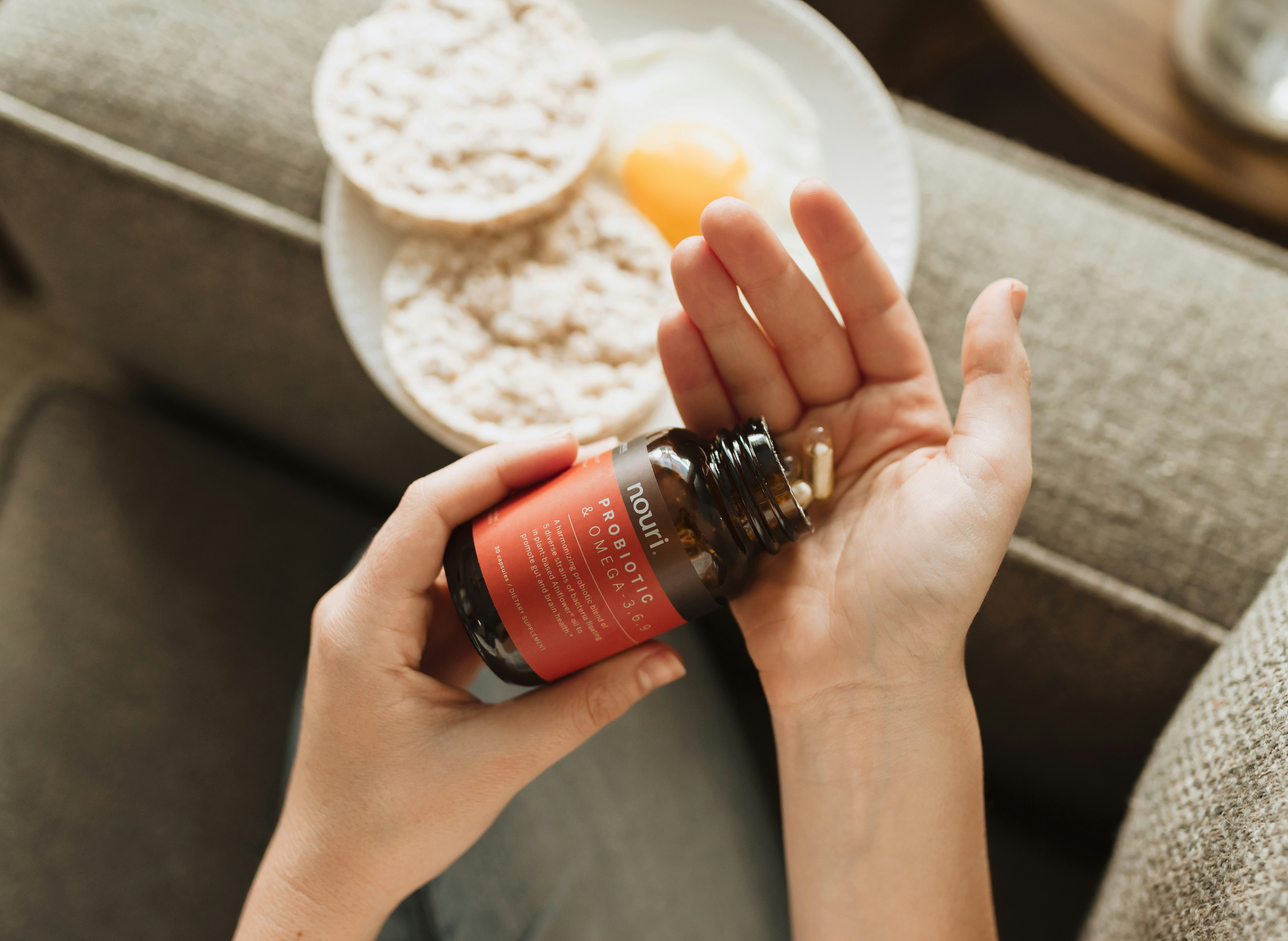 A person taking daily supplement capsules alongside breakfast.