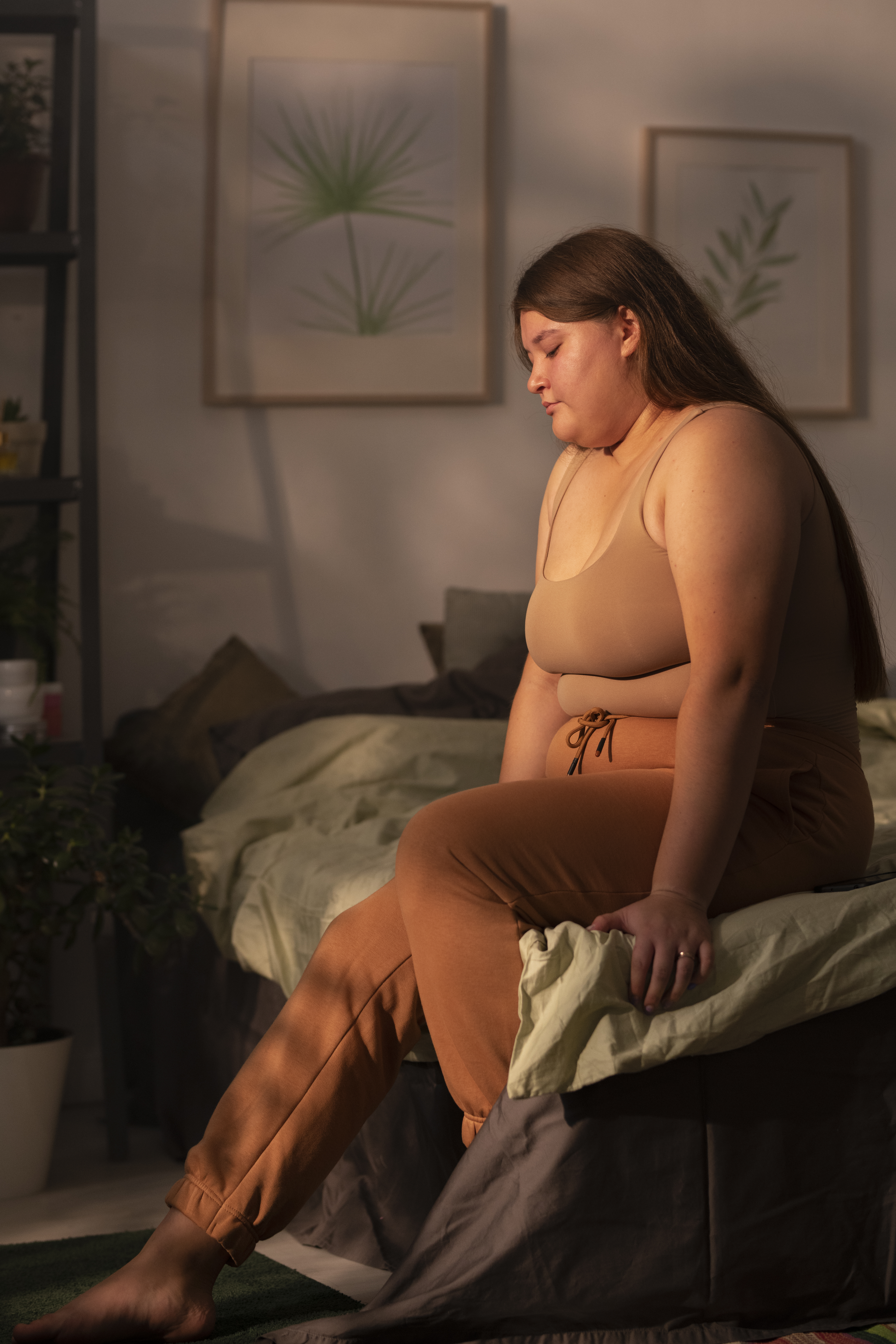 A woman sitting alone on the edge of a bed in low evening light.